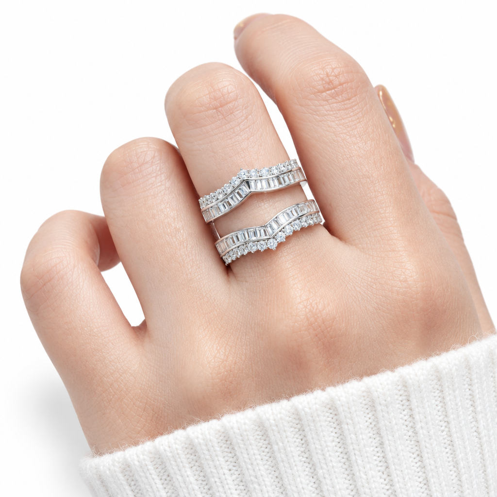 A close-up of a hand wearing two stacked silver bands with baguette-cut clear stones, photographed against a clean white background.