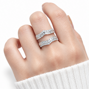 A close-up of a hand wearing two stacked silver bands with baguette-cut clear stones, photographed against a clean white background.
