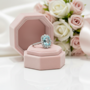 Ring with a blue gemstone on a pink cushion, surrounded by pink and white roses.