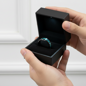 Person holding a black jewelry box with a ring inside against a neutral background