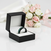Black ring box with a ring inside, placed on a white surface with flowers in the background.