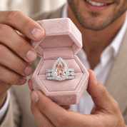 A close-up lifestyle shot of a man holding an open pink velvet ring box, showcasing a pear-cut pink gemstone ring with diamond accents.