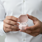 Person holding a pink jewelry box with silver earrings inside against a white background