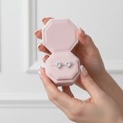 Heart-shaped earrings in a pink hexagonal jewelry box held by a hand.