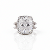 A cushion-cut diamond ring with a halo setting and a split shank band, shown on a clean white background with a soft reflection.