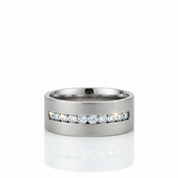 A silver-toned metal band ring featuring a channel-set row of round clear gemstones across the front, photographed on a clean white background with a soft reflection below.