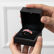 Rose gold ring with gemstones in a black jewelry box held by hands against a white background