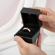 Rose gold ring in a black box held by hands against a light background