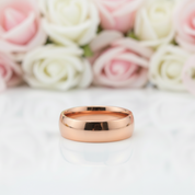Rose gold ring on a white surface with pink and white roses in the background