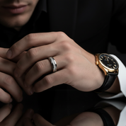 Close-up of a person's hand wearing a gold watch and silver ring on a dark background