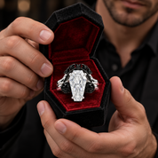 A close-up lifestyle shot of a man holding an open black velvet ring box. The ring features a large, coffin-shaped clear gemstone in a silver-toned setting with black accents on either side, held between his hands.