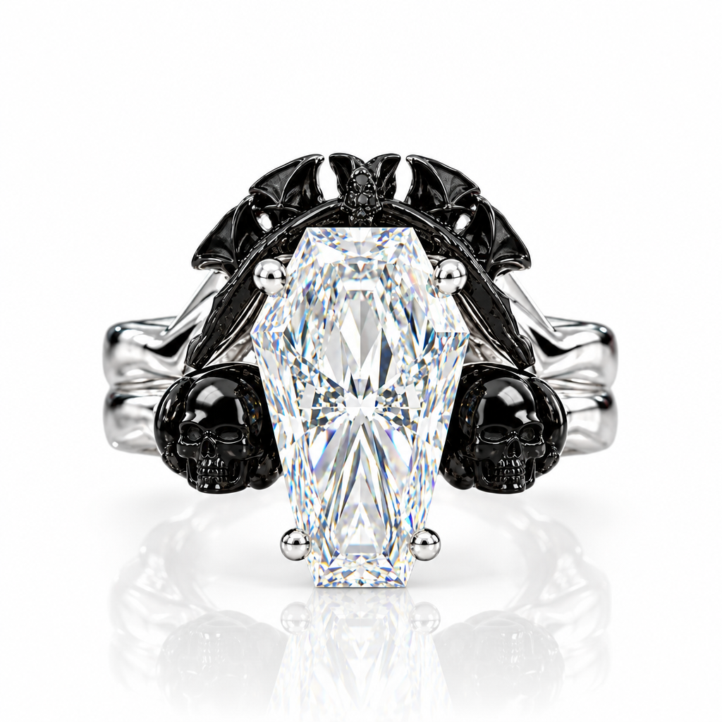 A gothic-style ring featuring a large coffin-shaped clear gemstone in a silver-toned setting, flanked by black skulls and bat wings on a white reflective background.