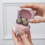 Hand holding a pink jewelry box with decorative earrings inside against a light background