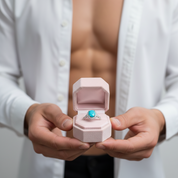 Person holding a ring with a blue stone in an open box, wearing a white shirt.