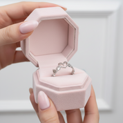 Hand holding a pink jewelry box with a silver ring inside on a white background