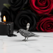 Silver bird-shaped pendant with red and black roses and a candle in the background