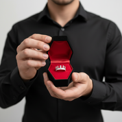 Person holding a black jewelry box with a red interior containing a silver ring.