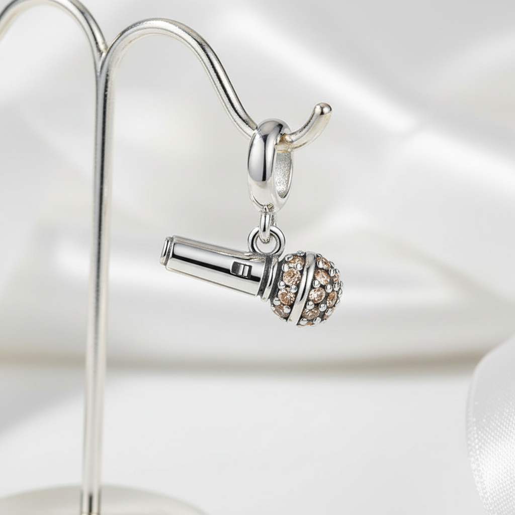 Silver microphone charm with clear stones on a reflective surface