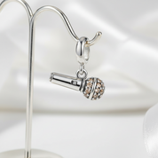 Silver microphone charm with clear stones on a reflective surface
