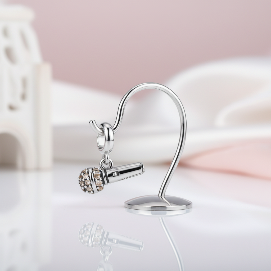 Silver microphone-shaped earring with a small gemstone on a reflective surface.