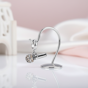 Silver microphone-shaped earring with a small gemstone on a reflective surface.