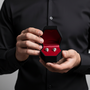 Person holding a black jewelry box with skull-shaped earrings on a neutral background