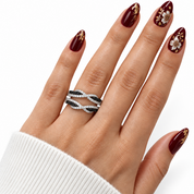A close-up of a hand wearing a double-band ring with pavé-set black and white stones, against a clean white background. The nails are decorated with dark burgundy polish and gold floral designs.