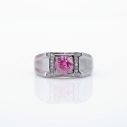 A silver-toned ring featuring a central round pink gemstone surrounded by a double-row border of small clear stones, set against a clean white background with a soft reflection below.