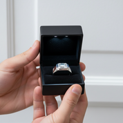 Silver ring with a large diamond in a black box held by a hand against a white background