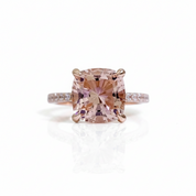 A cushion-cut pink diamond ring with a rose gold setting and a pavé band with small clear diamonds, shown on a white background with a soft reflection.