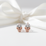 Rose gold skull earrings with clear gemstones on a soft white background