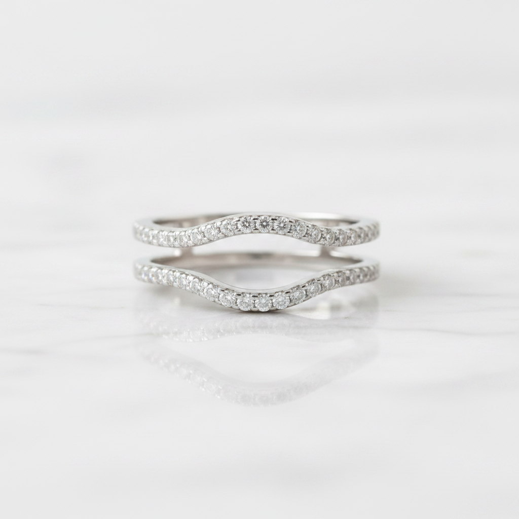 Two silver wavy band rings set with small clear stones, displayed on a white marble surface with a soft reflection.