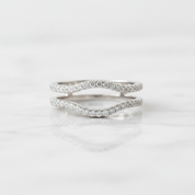 Two silver wavy band rings set with small clear stones, displayed on a white marble surface with a soft reflection.