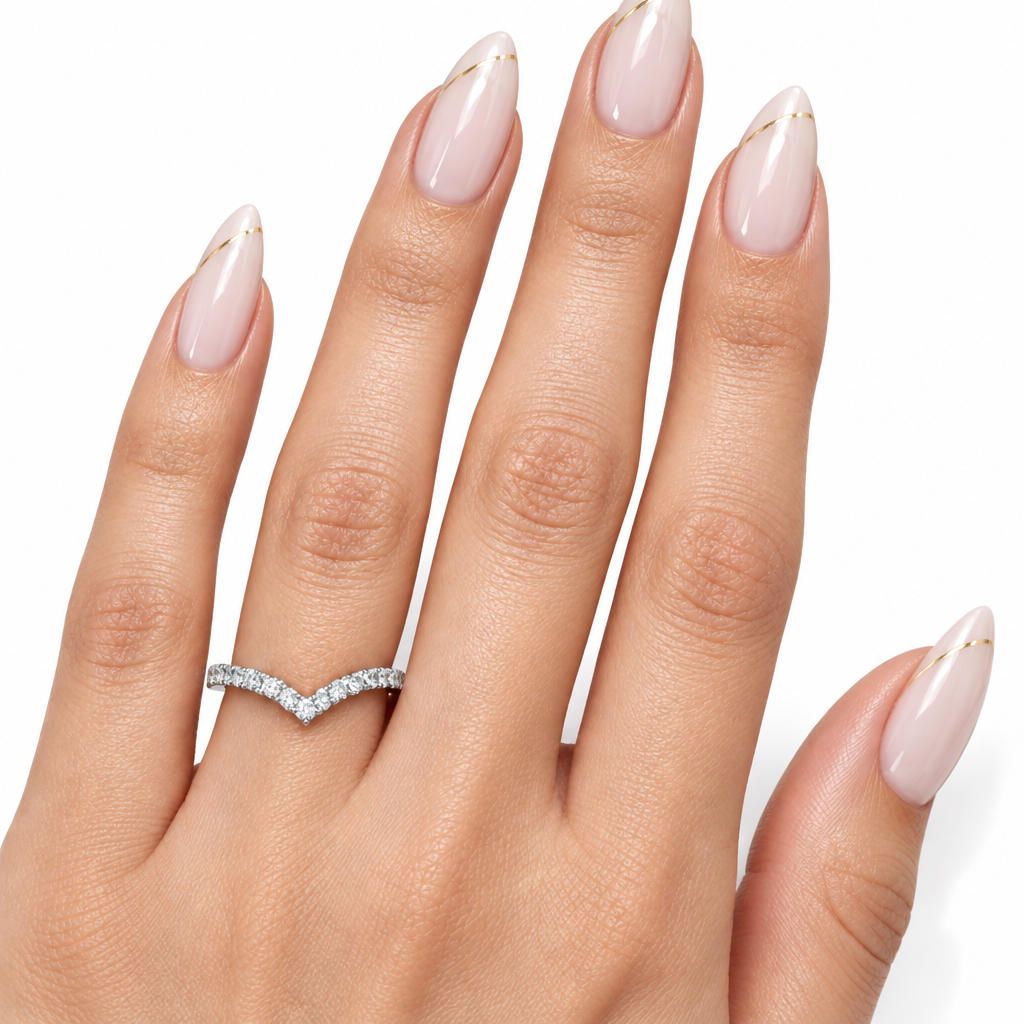 A close-up of a hand with long, pale pink manicured nails wearing a silver chevron ring set with small clear stones. The hand is shown against a clean white background.