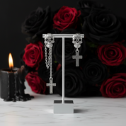Silver skull and cross earrings on a stand with red roses and a candle in the background
