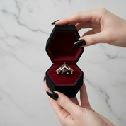 Black ring box with a ring inside, held by a hand against a marble background