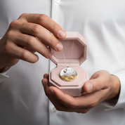 Person holding a pink jewelry box with a gold and silver pendant inside.