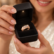 A close-up lifestyle shot of a woman holding an open black jewelry box that displays a rose gold ring with a row of clear gemstones.