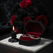 Open jewelry box with a silver chain, black candle, and red roses on a dark background