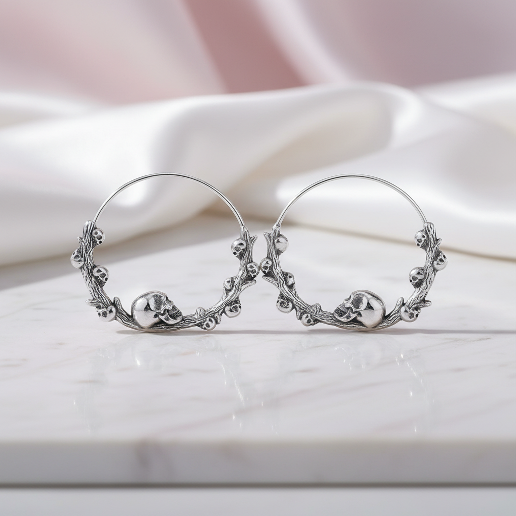 Silver hoop earrings with skull designs on a white surface