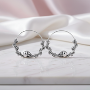 Silver hoop earrings with skull designs on a white surface