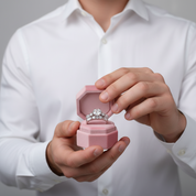 Person holding a pink jewelry box with a ring inside, wearing a white shirt.