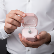 Person holding a pink jewelry box with a silver necklace featuring a teardrop pendant.