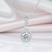 Silver teardrop-shaped pendant with clear gemstone on a soft pink background