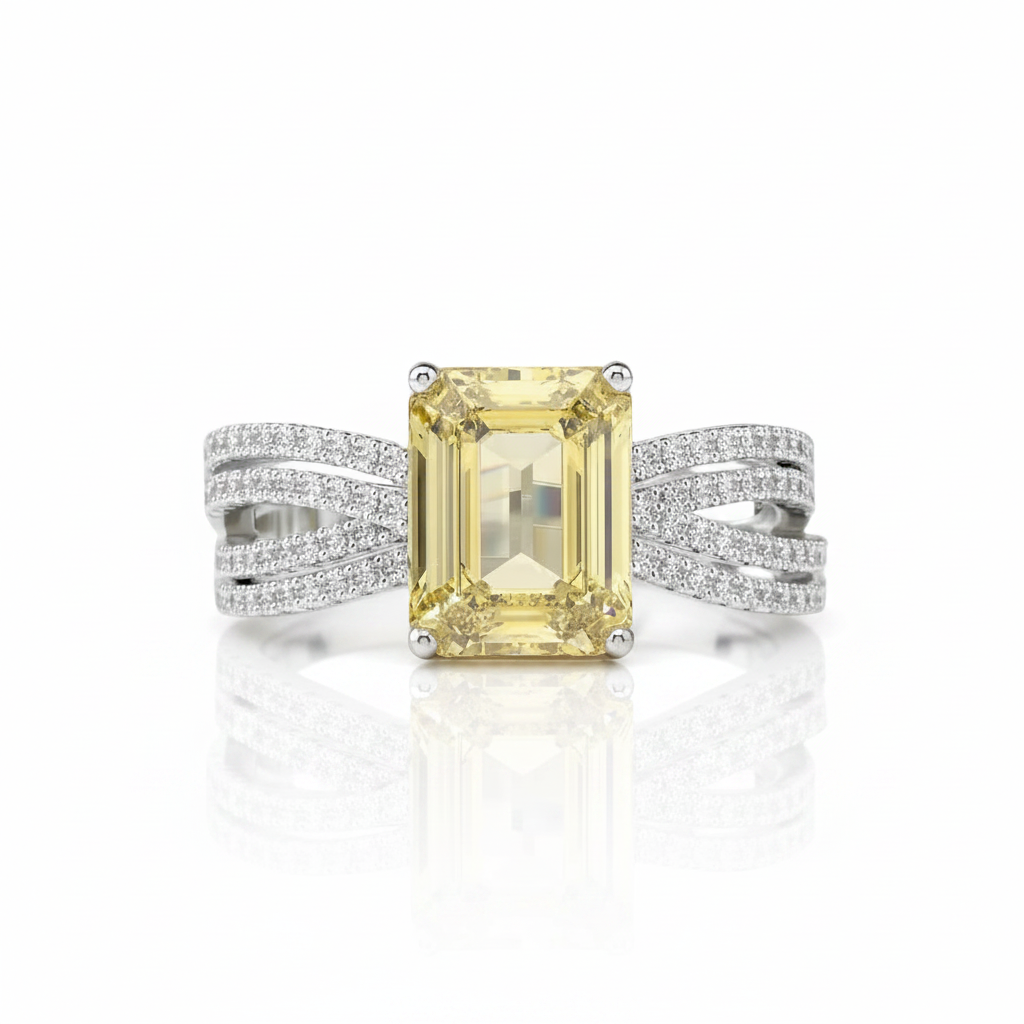 An emerald-cut yellow diamond ring set in a silver-toned band with pavé-set accent diamonds, shown on a clean white background with a soft reflection.