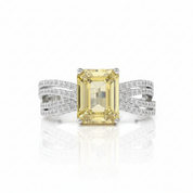 An emerald-cut yellow diamond ring set in a silver-toned band with pavé-set accent diamonds, shown on a clean white background with a soft reflection.