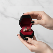 Person holding a black jewelry box with a red interior containing a ring.